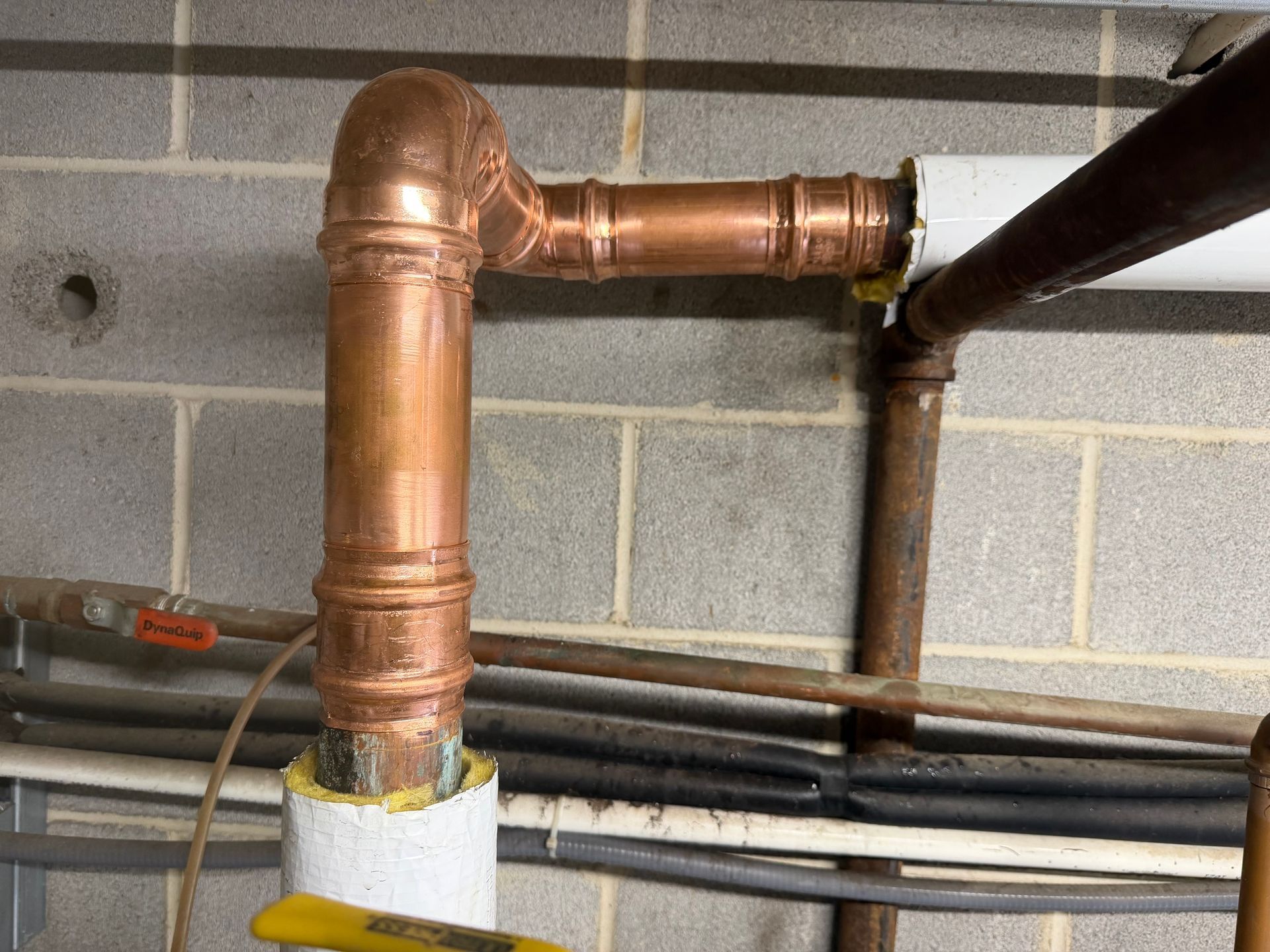 Copper plumbing pipe elbow and vertical section against a cinderblock wall in a basement.