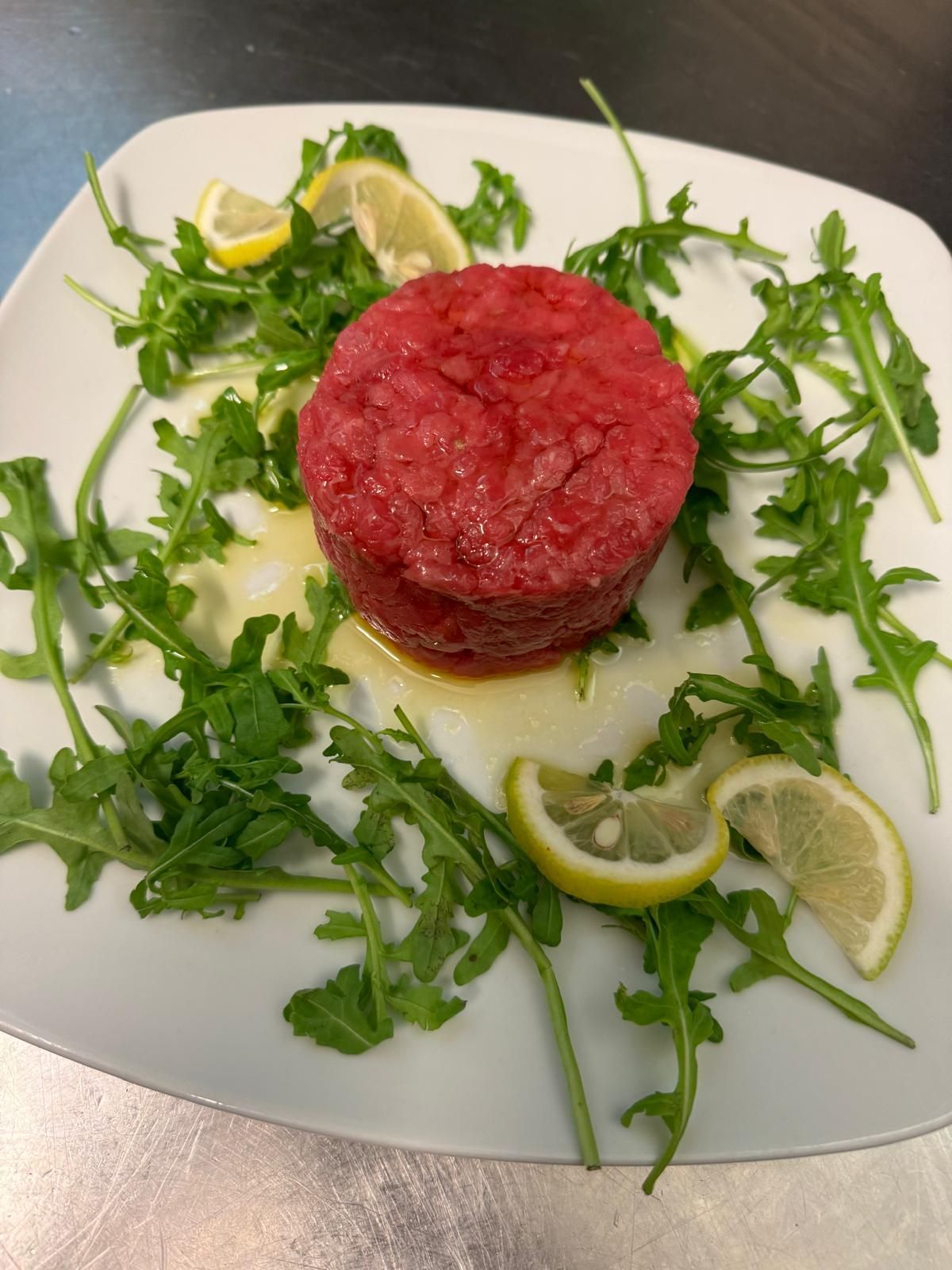 Tartare di barbabietola su un piatto bianco con rucola e spicchi di limone