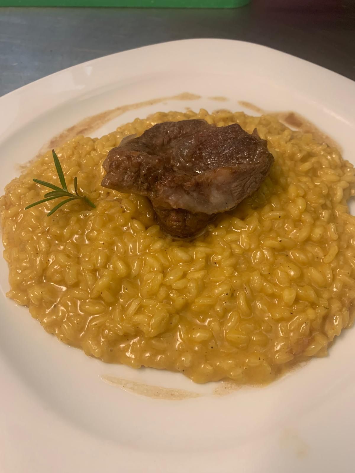 Piatto di cremoso risotto allo zafferano guarnito con un pezzo di carne scottato e un rametto di rosmarino