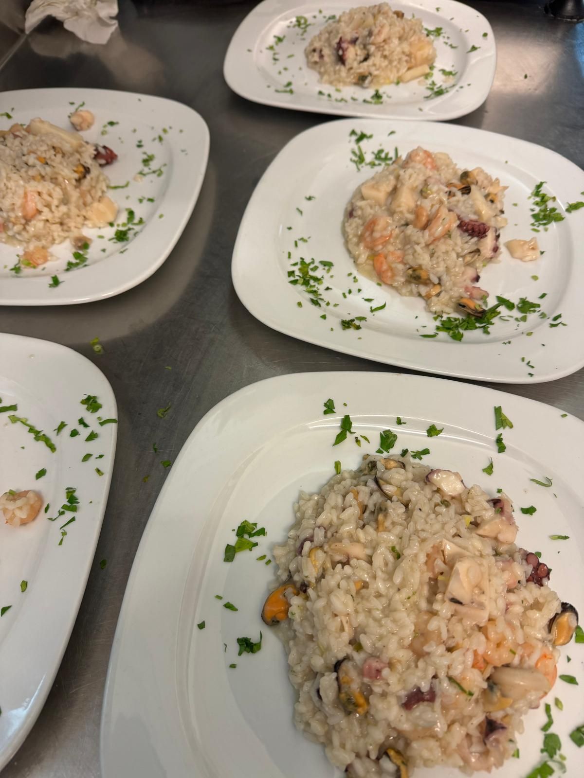 Piatti di cremoso risotto guarnito con erbe aromatiche, disposti sul bancone della cucina.