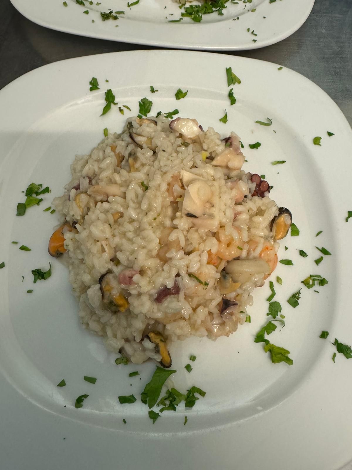 Piatto di cremoso risotto ai frutti di mare guarnito con prezzemolo su un piatto bianco.