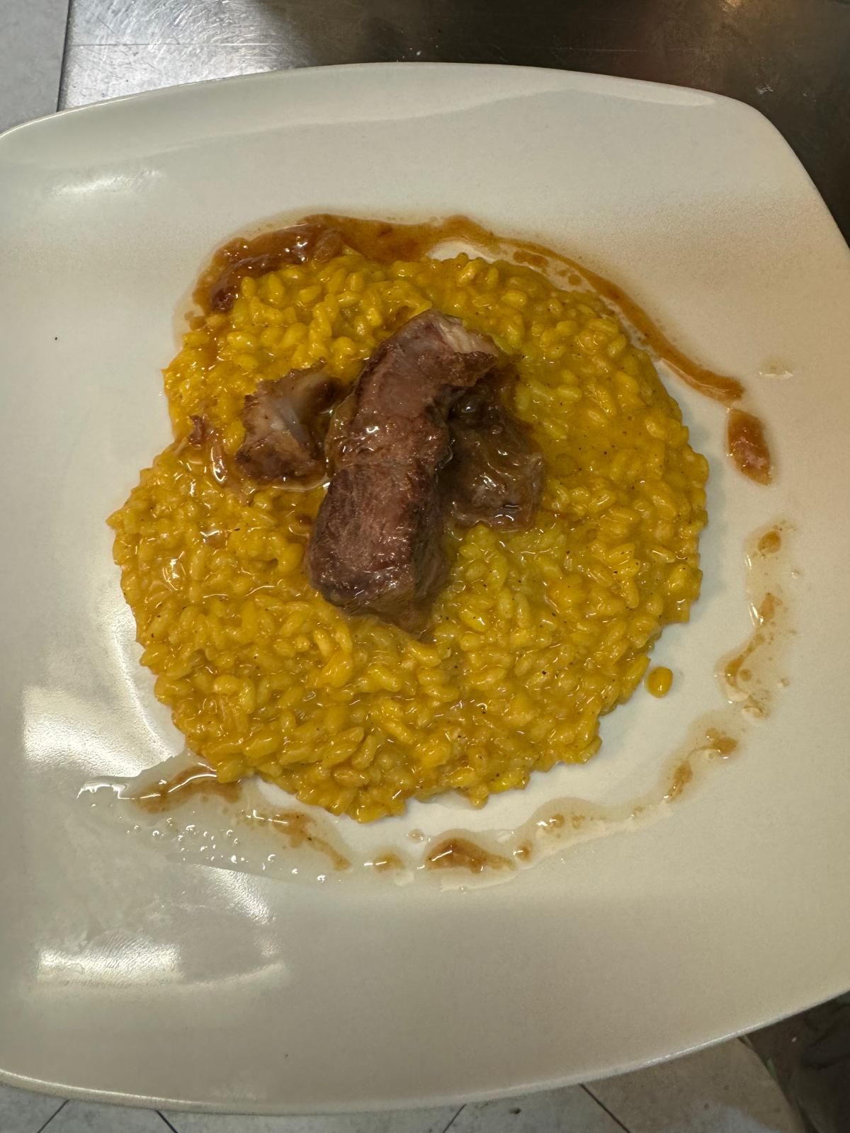 Piatto di risotto giallo con due pezzi di salsiccia su un piatto bianco