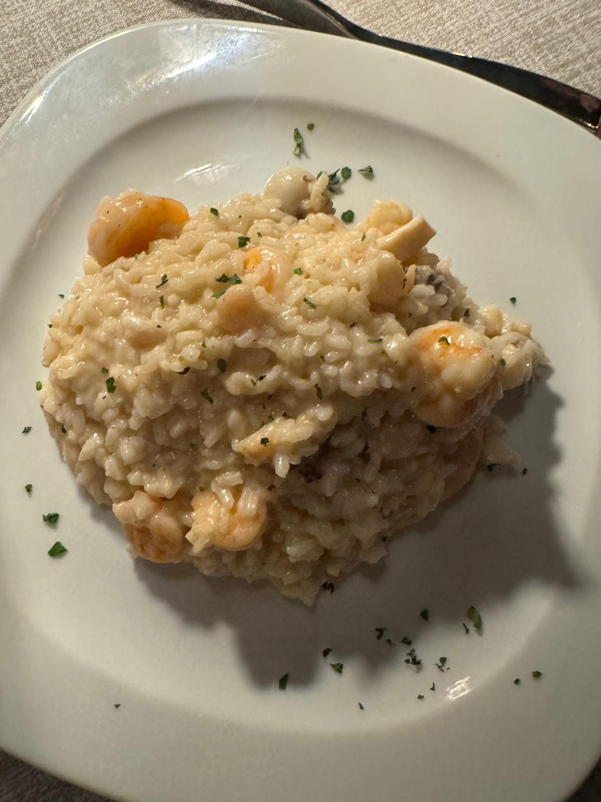 Un piatto di cremoso risotto ai gamberi guarnito con erbe aromatiche, servito su un piatto bianco.