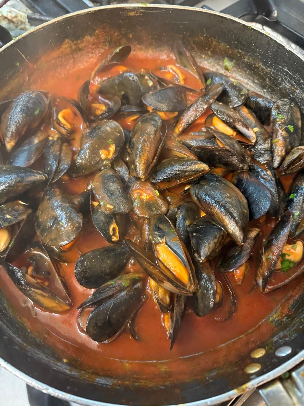 Pentola di cozze in salsa di pomodoro, con i gusci aperti sul fornello.