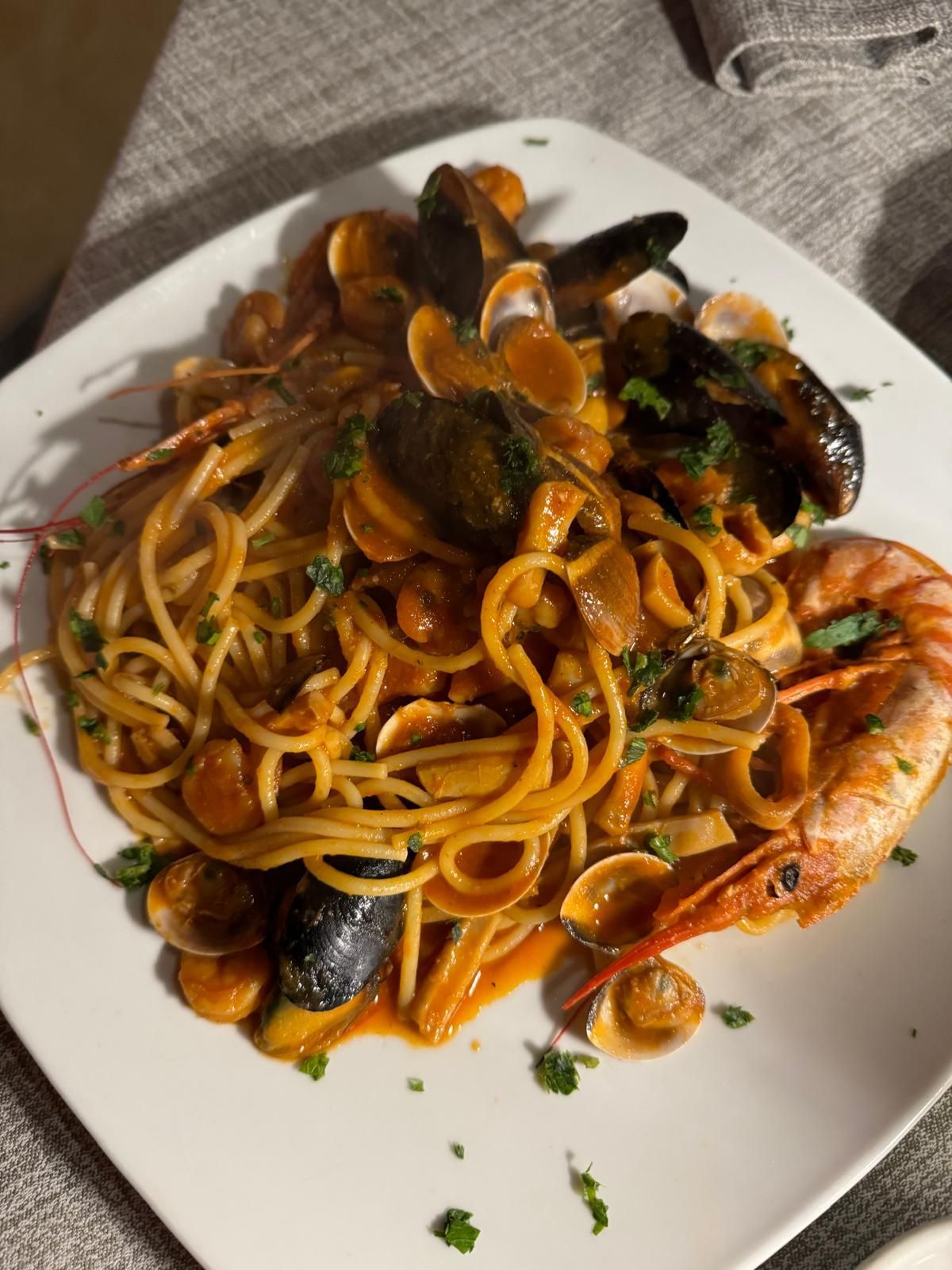 Spaghetti con gamberi, cozze e pomodorini su un piatto bianco con guarnizione di erbe aromatiche.