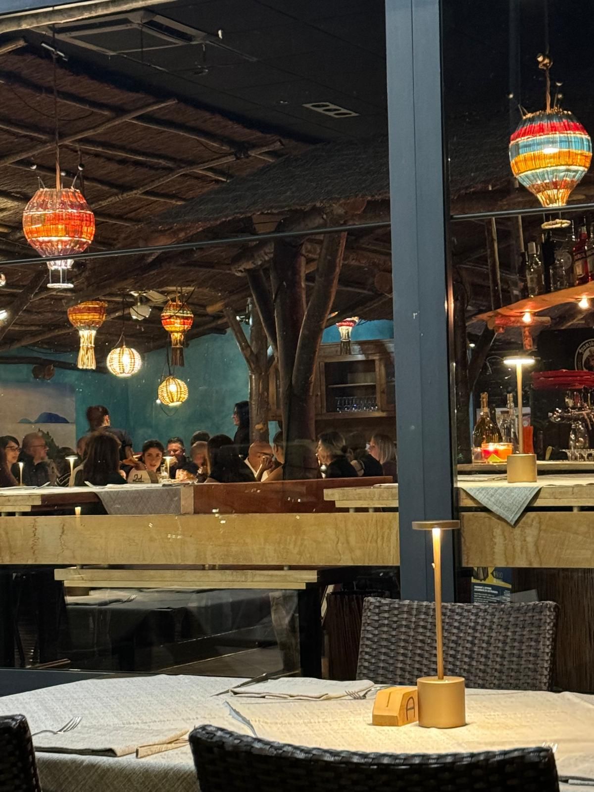 Ristorante con luci soffuse, lanterne appese, clienti seduti ai tavoli e un'atmosfera calda e accogliente.