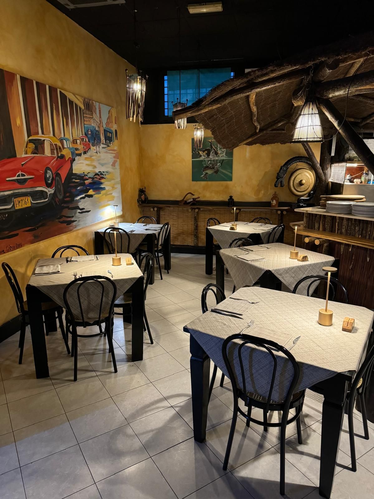Caffè vuoto con sedie nere, tovaglie bianche, arredamento vintage e un murale raffigurante un'auto da corsa sulla parete.
