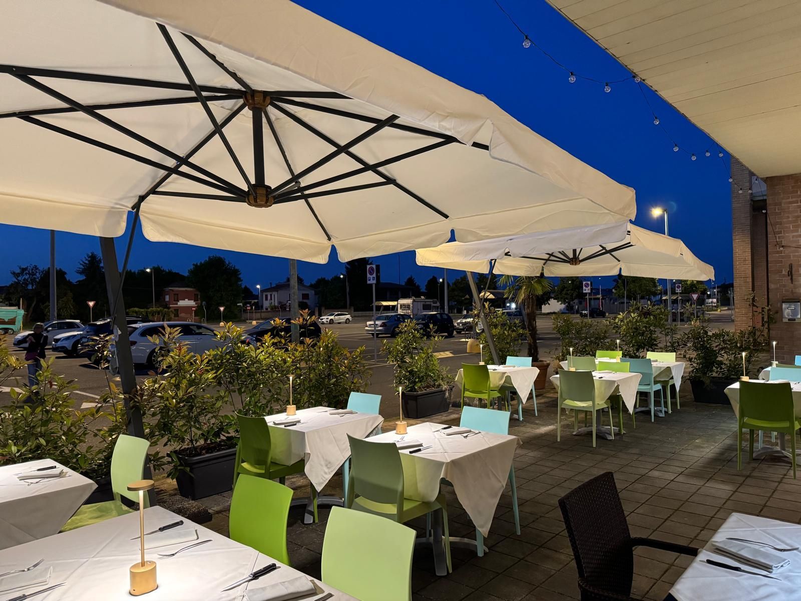 Terrazza esterna del ristorante con tavoli bianchi, sedie verdi e grandi ombrelloni al crepuscolo
