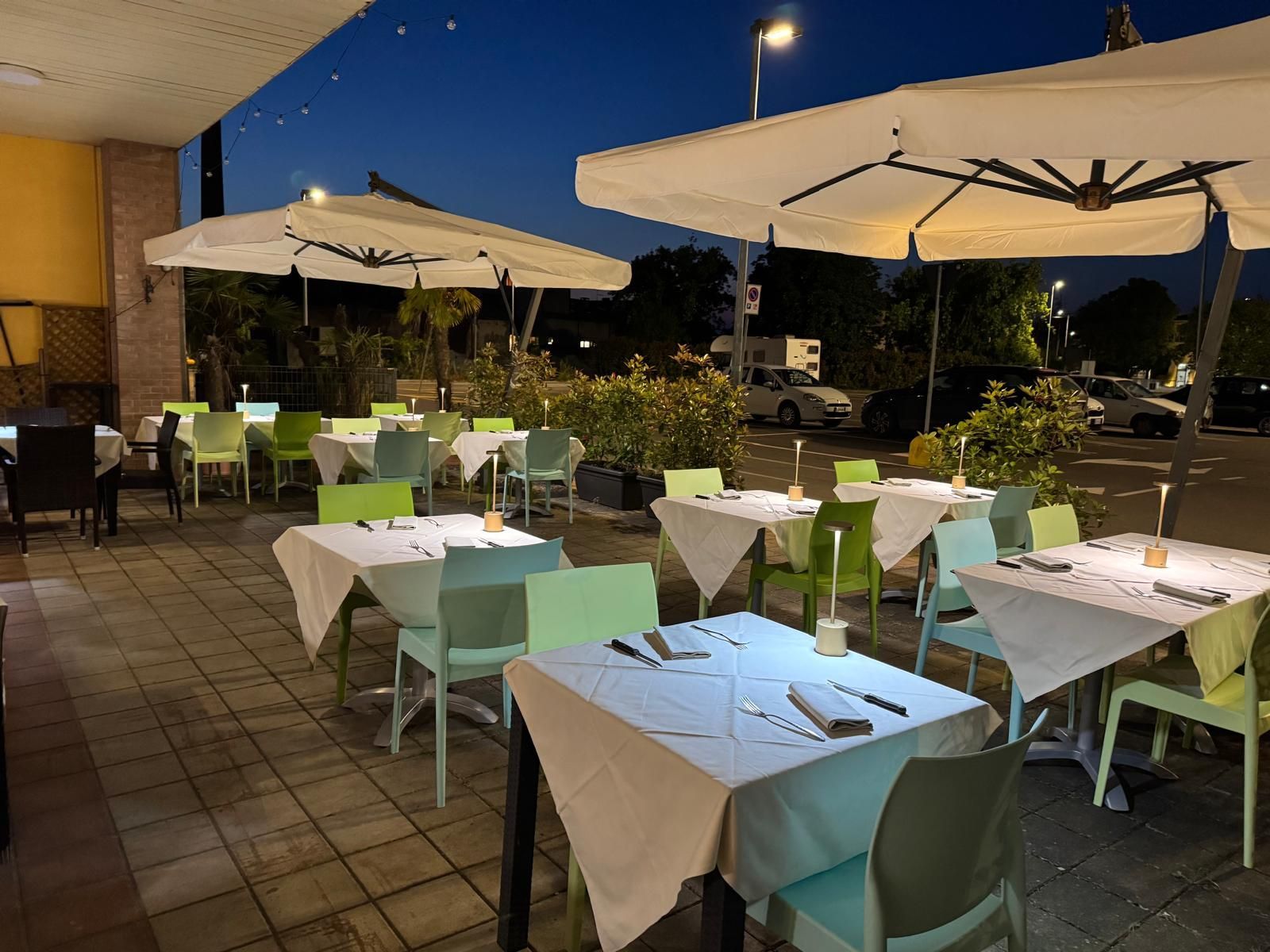 Terrazza esterna del ristorante con ombrelloni bianchi, sedie turchesi e tavoli apparecchiati al crepuscolo.