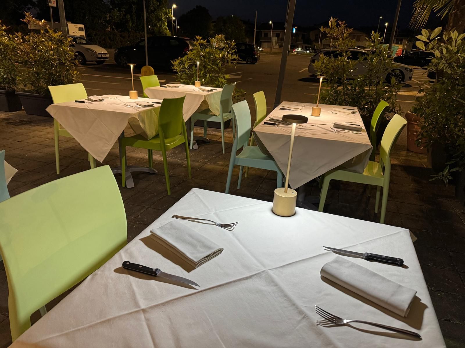 Tavolini da caffè all'aperto apparecchiati per la cena serale con tovaglie bianche e sedie verde chiaro