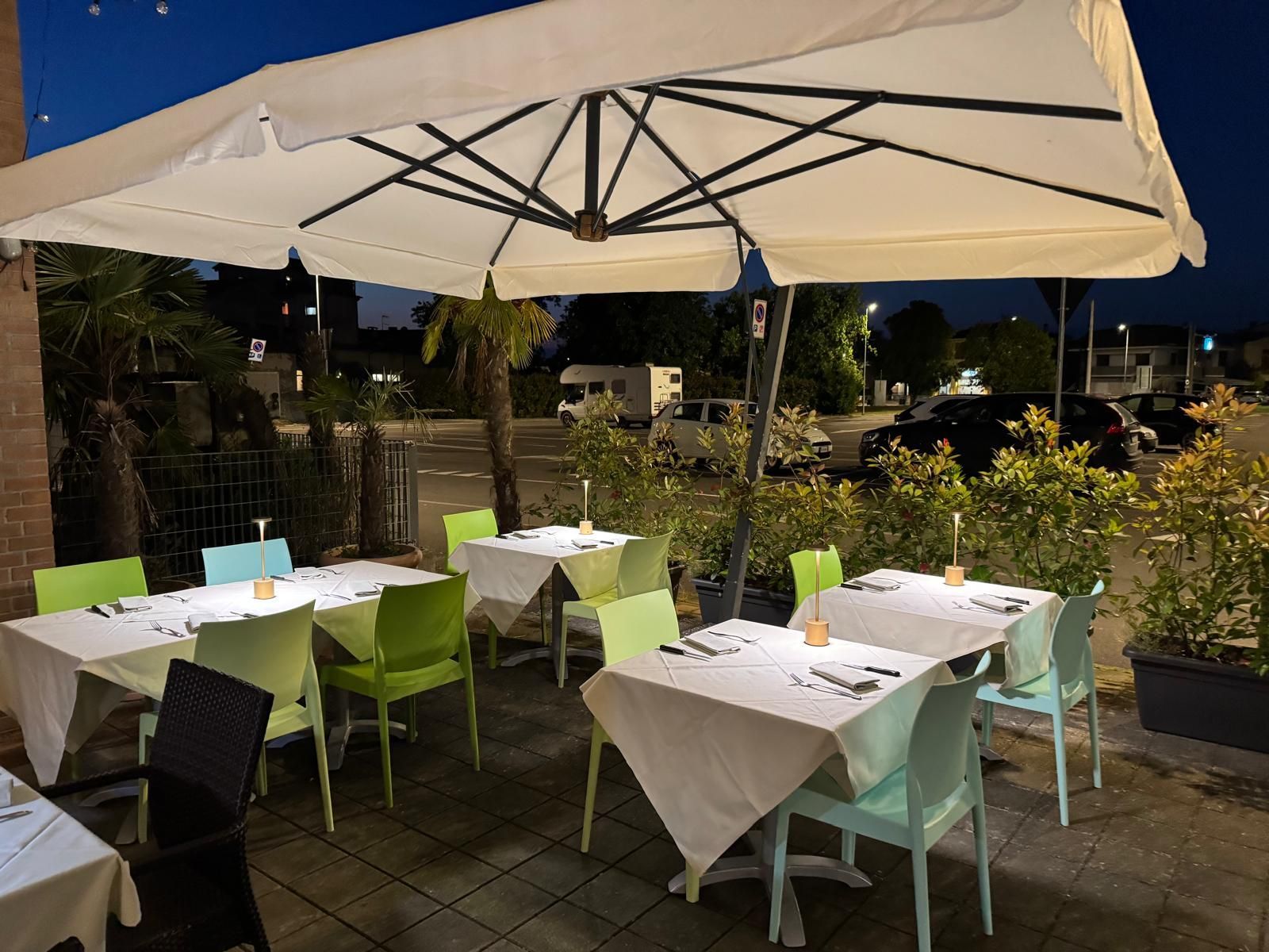 Il patio esterno del caffè di sera, con tavolini bianchi, sedie color pastello e un grande ombrellone color crema.