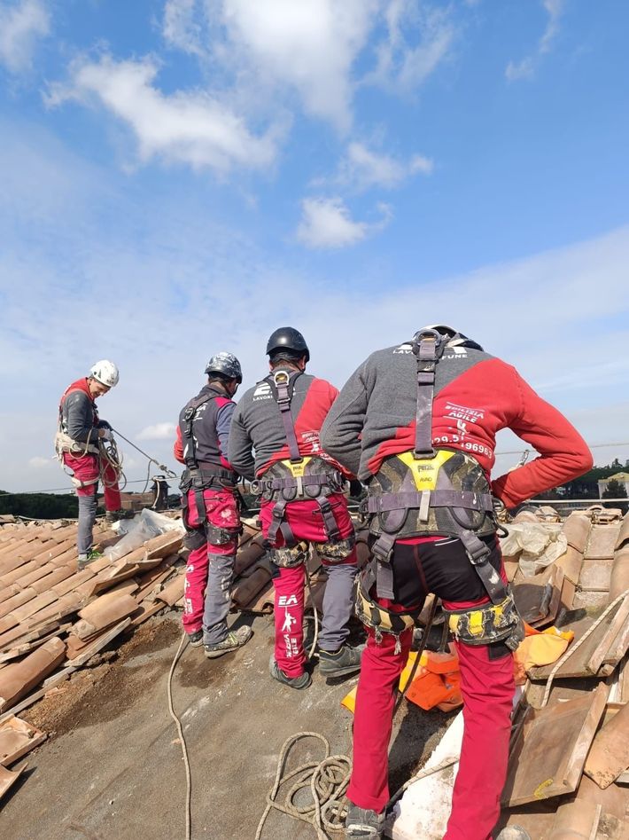 Alpinisti vestiti di rosso e nero sono in piedi su una cresta rocciosa, sotto un cielo azzurro con nuvole.
