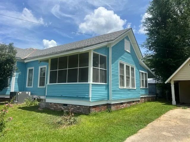 Blue house with white trim and screened porch on a grassy lot under a partly cloudy sky