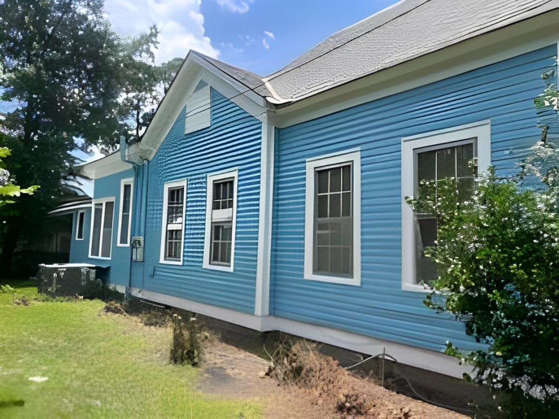Blue house exterior with white trim, multiple windows, and a small front porch in a sunny yard