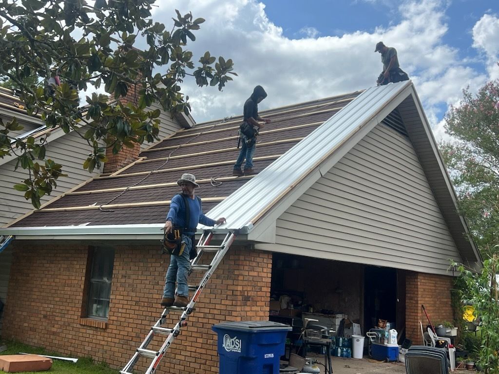Workers on a house roof replacing shingles and installing a metal roof panel.