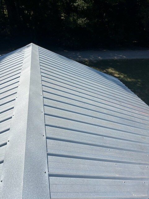 White metal roof ridge in the foreground with trees and a shaded yard in the background