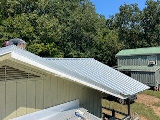 Metal roof installed on a beige building beside a green house under trees
