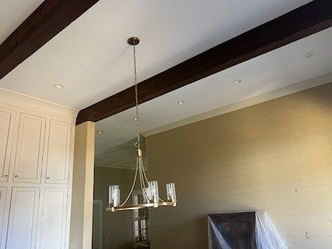 Modern dining room with a chandelier, dark ceiling beams, and white built-in cabinets
