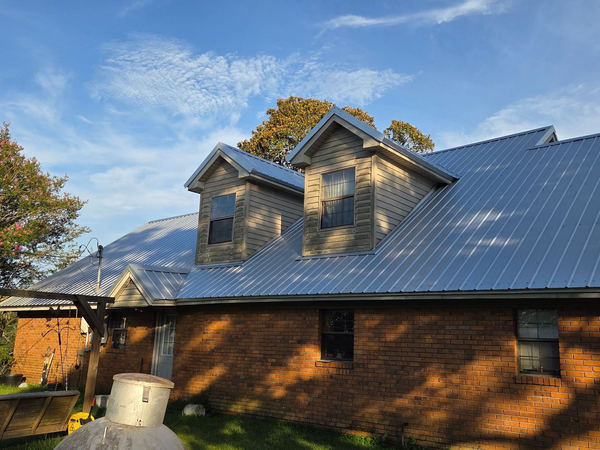 Brick house with a steep metal roof and dormer windows under a blue sky