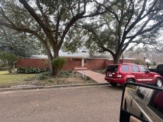 Brick house with large trees in front and a red SUV parked by the curb