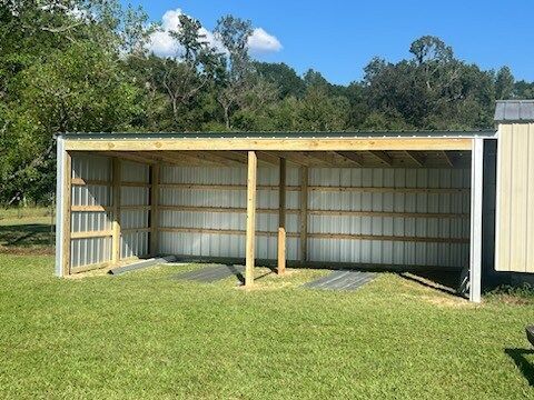 Open-sided metal shed with wooden frame in a grassy field under a blue sky