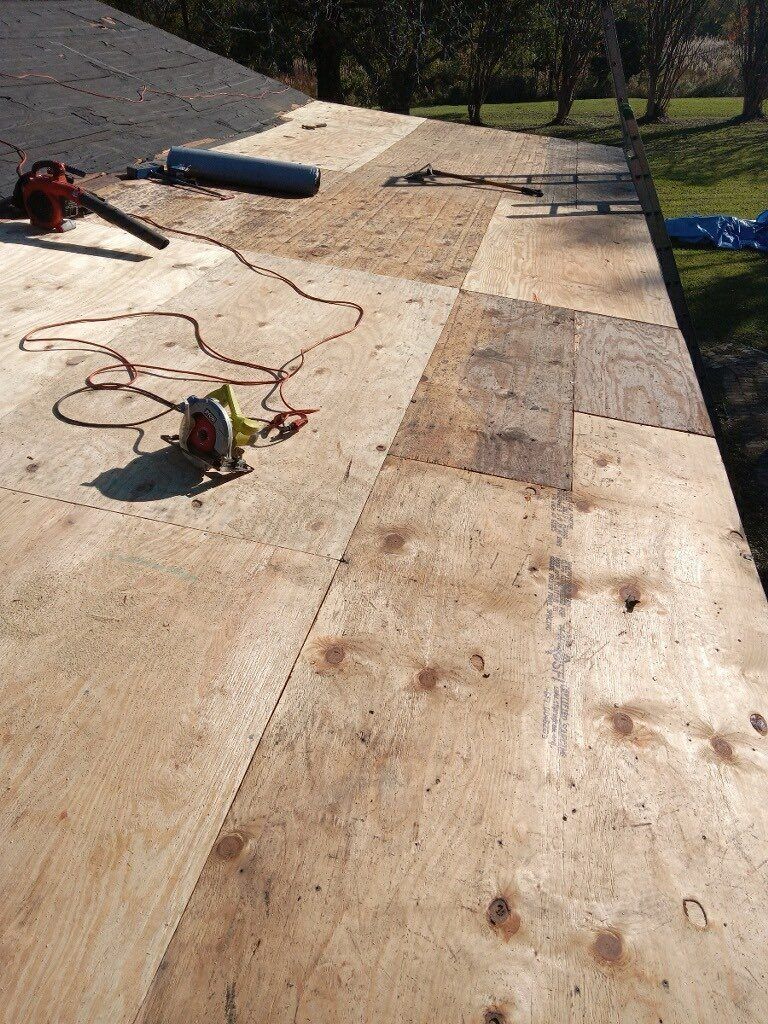 Workers repairing a flat roof with tools, tarps, and wood panels in sunlight