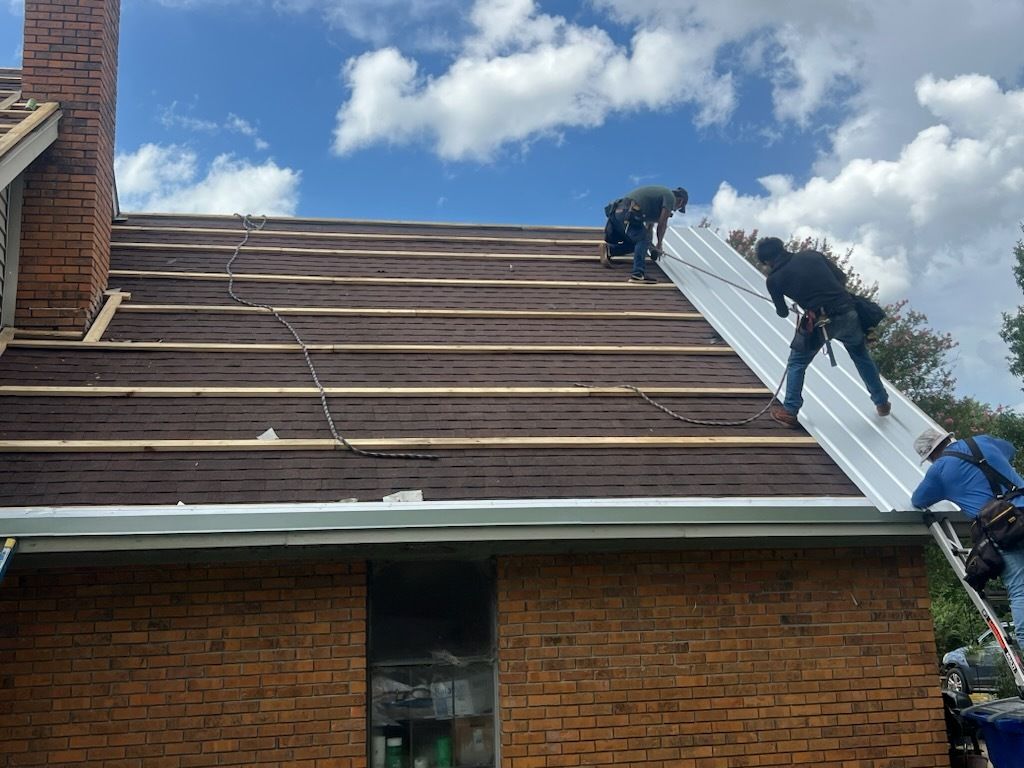 Roofers installing underlayment on a steep brick house roof under a blue sky