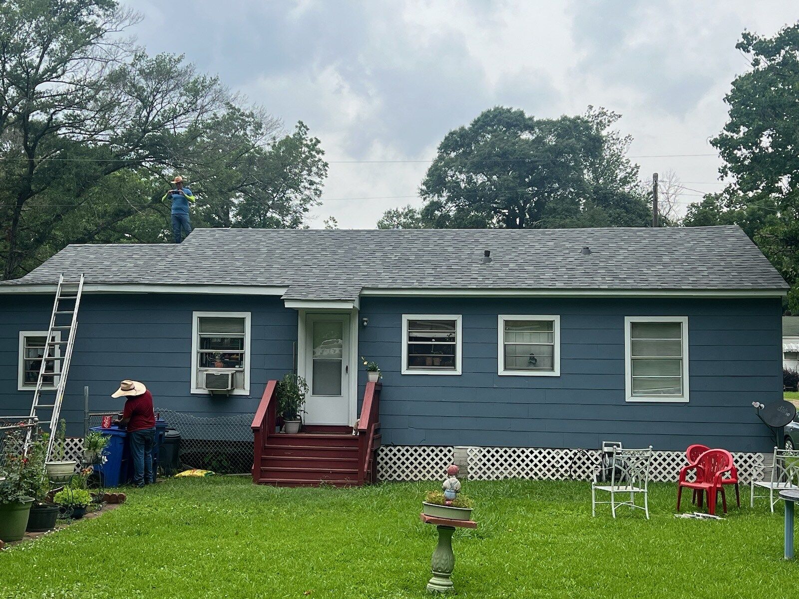 Blue single-story house with a small porch, ladder, and lawn ornaments in a grassy yard
