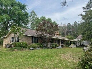 Single-story brick house with a front porch, surrounded by trees and a grassy yard