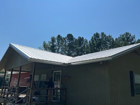 Small house with a white metal roof and porch under a clear blue sky.