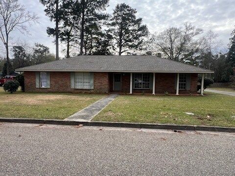Single-story brick house with front walkway, lawn, and trees on an overcast day