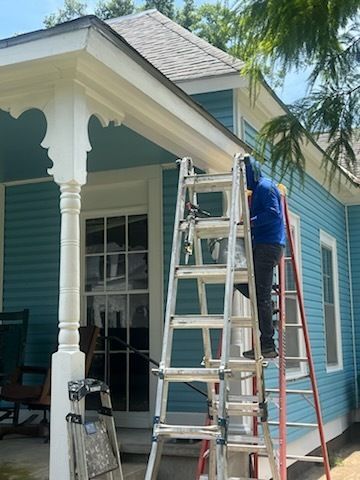 Worker on ladder painting blue house exterior by white porch