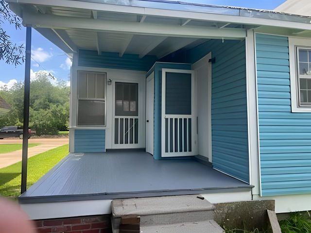 Blue house porch with open screen door, white railings, and front steps under a covered roof