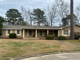 Single-story beige house with a front porch, lawn, and trees on an overcast day
