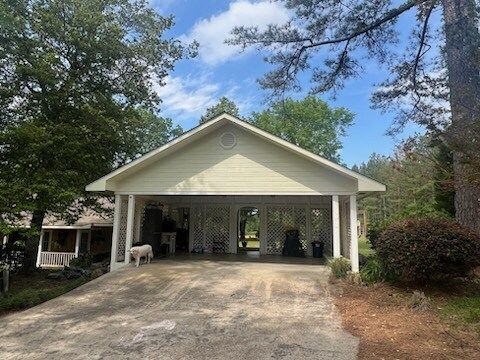 White carport with two parked vehicles, gravel driveway, and trees under a blue sky