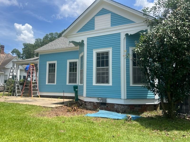 Blue house with white trim and gabled roof in a grassy yard under a sunny sky