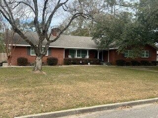 Single-story red brick house with a large front yard and leafless trees
