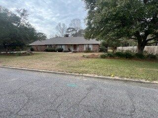 Single-story brick house with a large front yard and trees along a quiet street.