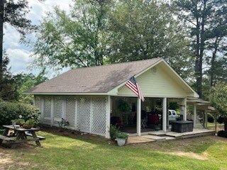 Small white patio pavilion with American flag, picnic table, and potted plants in a grassy yard.