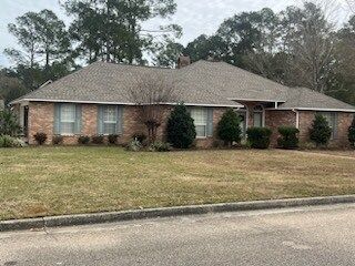 Single-story brick house with a gray roof, front lawn, and trees along a quiet street.