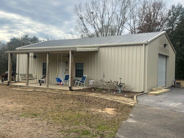 Beige metal house with front porch, blue chairs, and a garage, viewed from the driveway.