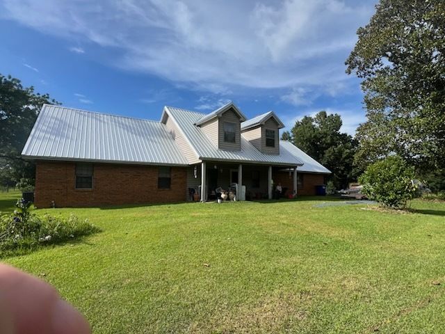 Brick house with white metal roof on a sunny lawn under a blue sky