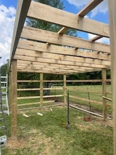 Partially built wooden shed frame with roof beams in a grassy yard, under a cloudy sky
