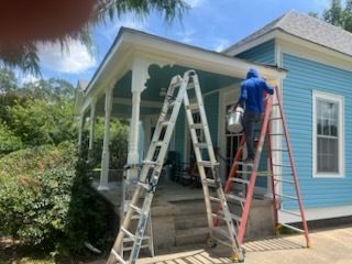 Two workers on ladders painting a blue house porch under a bright sky