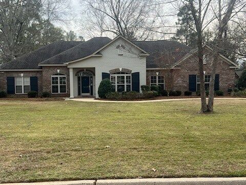 Single-story brick house with white front entry and large lawn under leafless trees