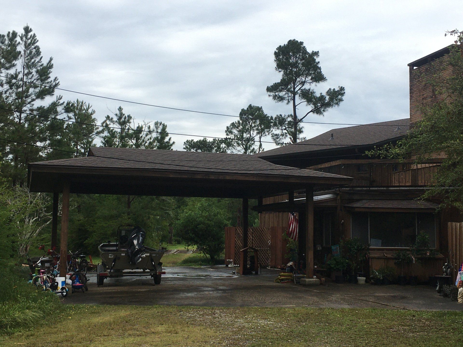 Brick house with carport, parked vehicle, and trees under a cloudy sky