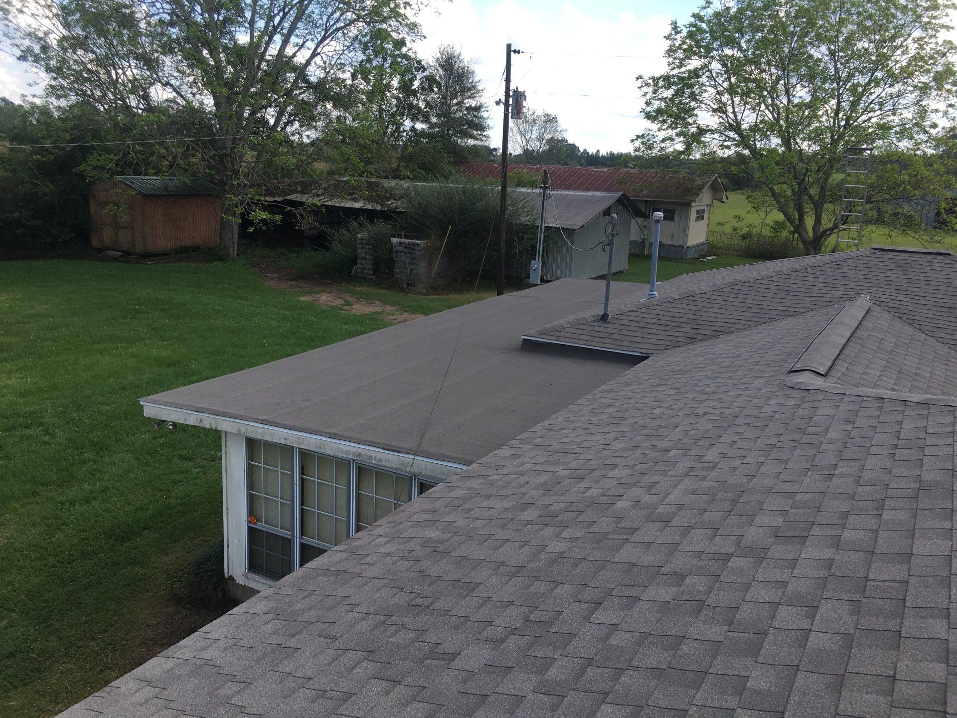 Rooftop view of a house with gray shingles, dormer windows, and a grassy yard with trees.