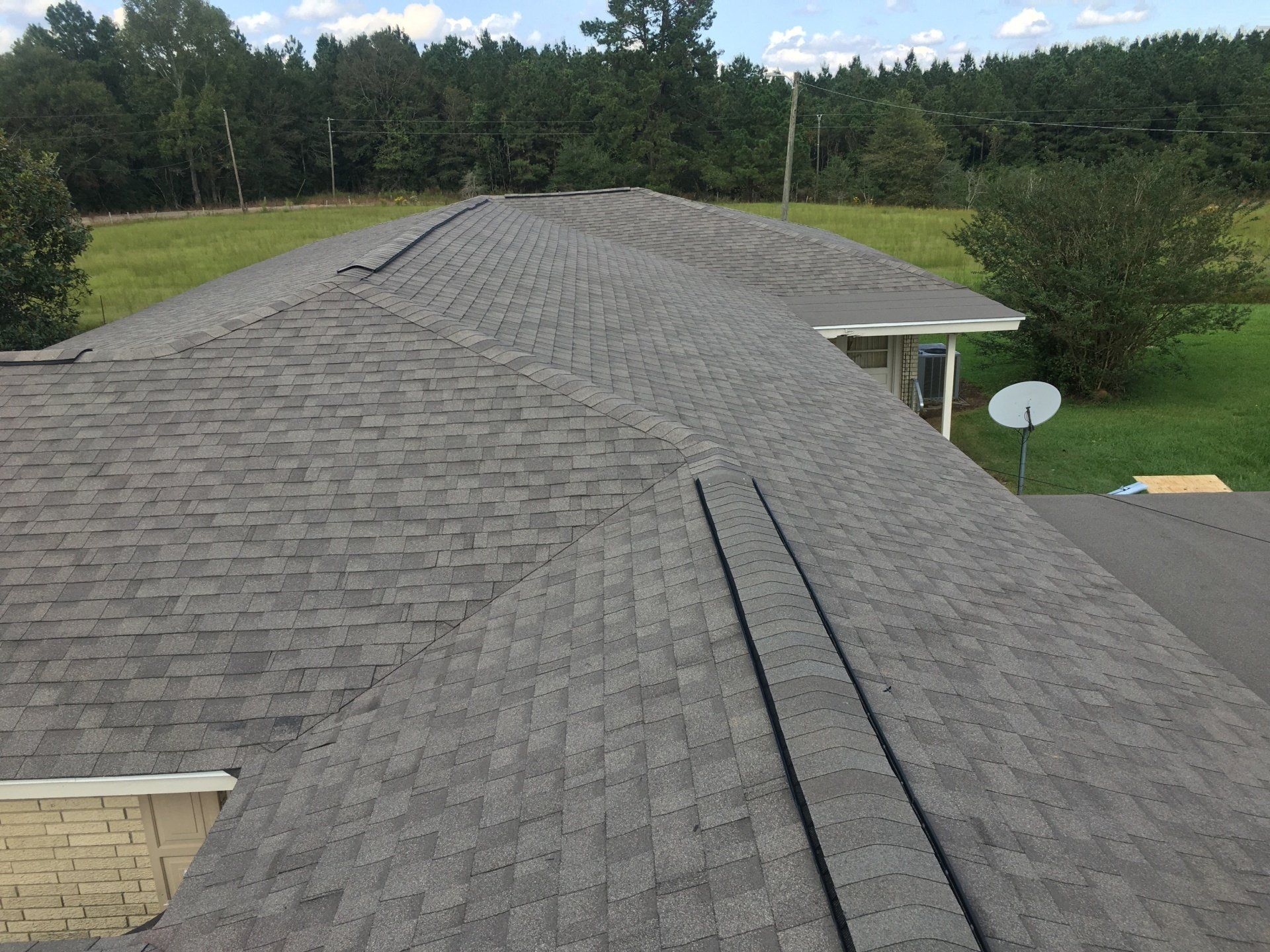 Gray shingled roof viewed from above, with trees and a small satellite dish in the background.