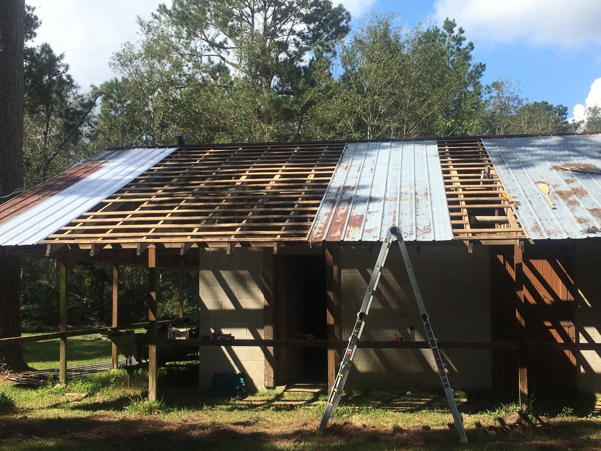 Partially stripped roof on a wooden house, with exposed rafters and corrugated metal panels under a blue sky