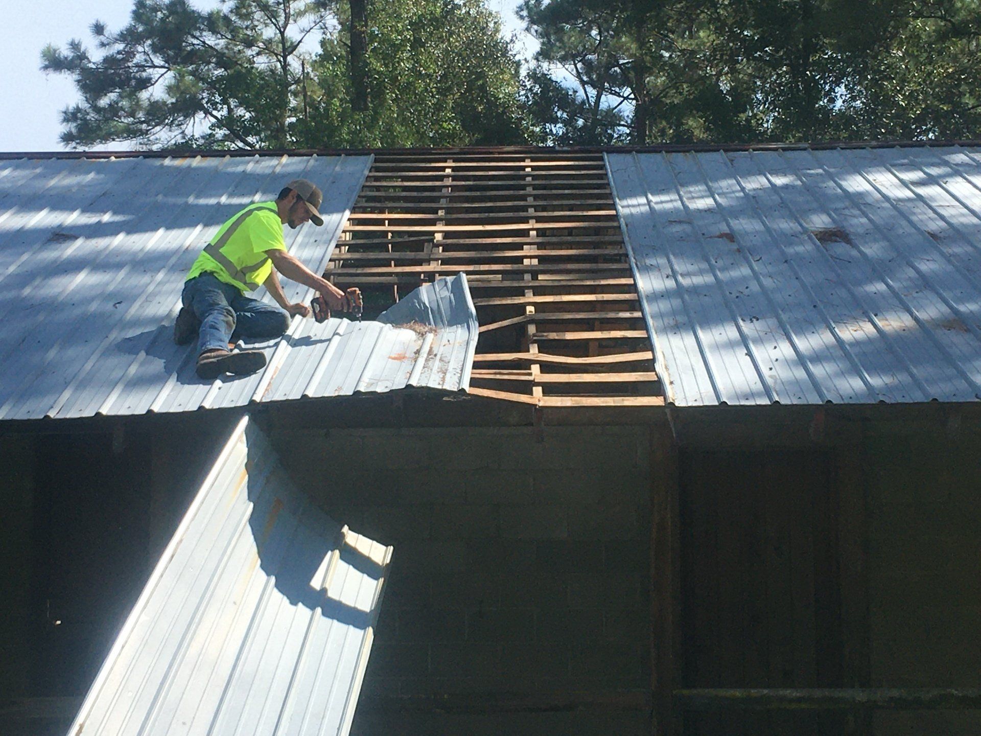 Worker repairing a metal roof, installing panels on a partially stripped rooftop.